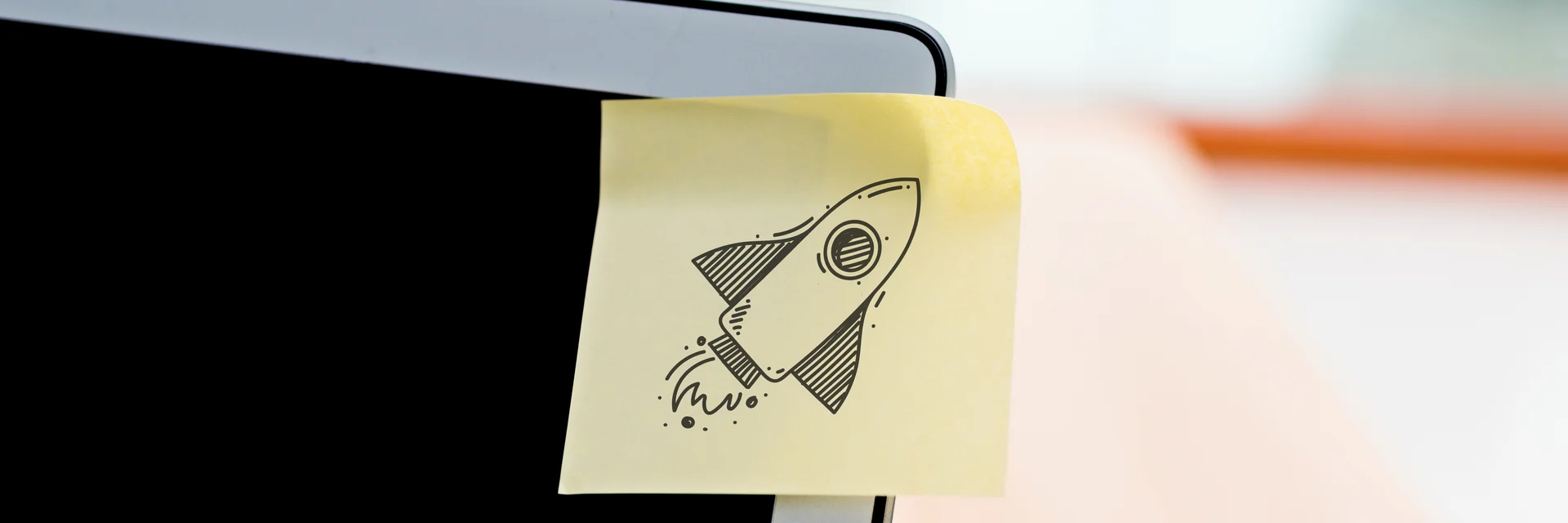 Man sieht die obere rechte Ecke eines Laptops, darauf ist ein Post-It mit einer gezeichneten Rakete