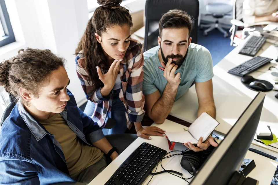Zwei Männer und eien Frau stehen in einer Gruppe um einen PC